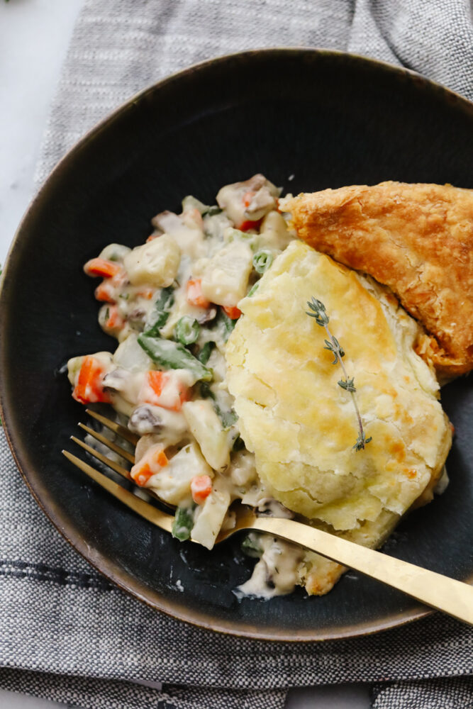 A slice of pot pie and fork on a black stoneware plate.