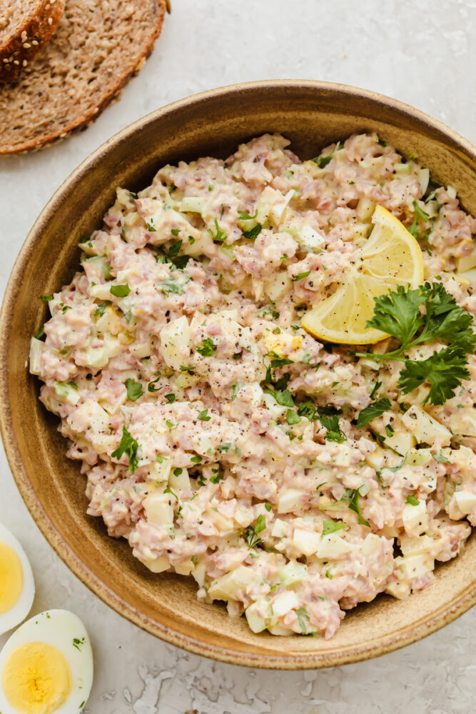 A bowl of ham salad garnished with a lemon. 