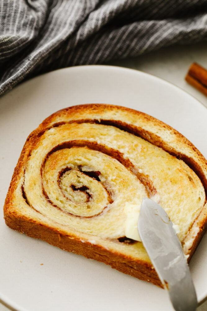 Butter being spread on a slice of the bread. 