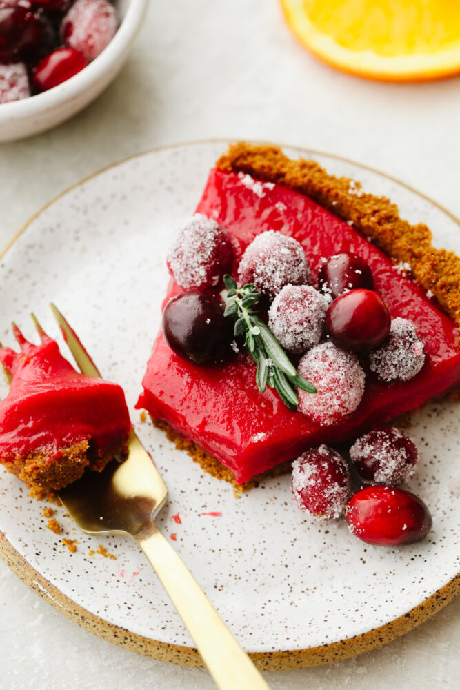 A slice of cranberry curd tart on a plate with a fork bite. 