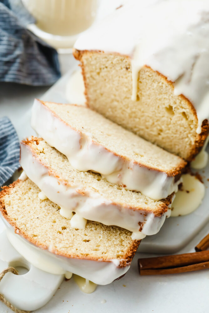 A loaf of eggnog quick bread sliced with an eggnog glaze on top. 