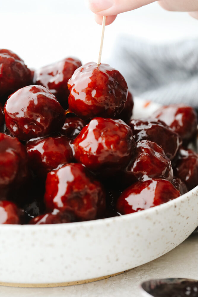 A bowl of grape jelly meatballs with a toothpick sticking in one of them. 