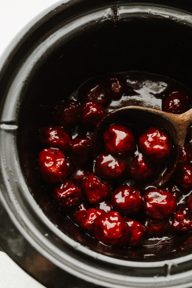 A crockpot filled with meatballs and a wooden spoon. 