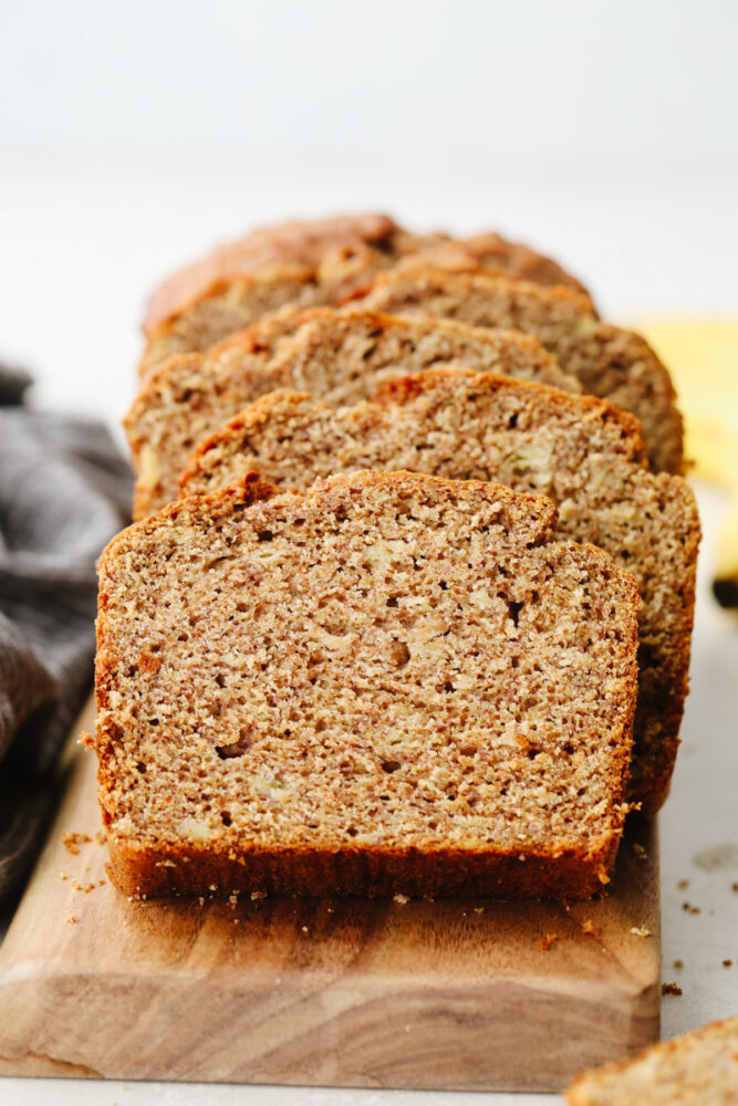 Banana bread sliced up on a wooden cutting board. 