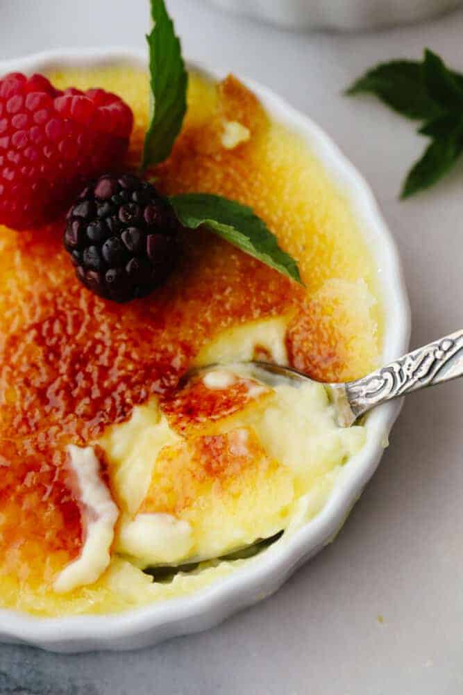 Creme brûlée in a ramekin with a spoon scooping some out. 