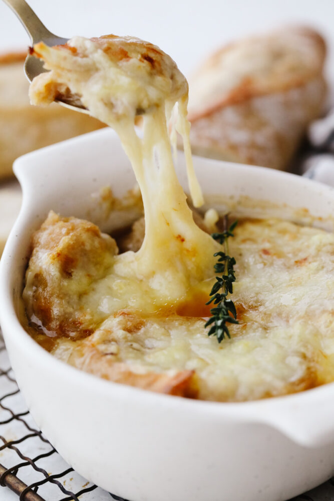 French Onion soup in a bowl topped with cheese and being scooped out with a spoon. 