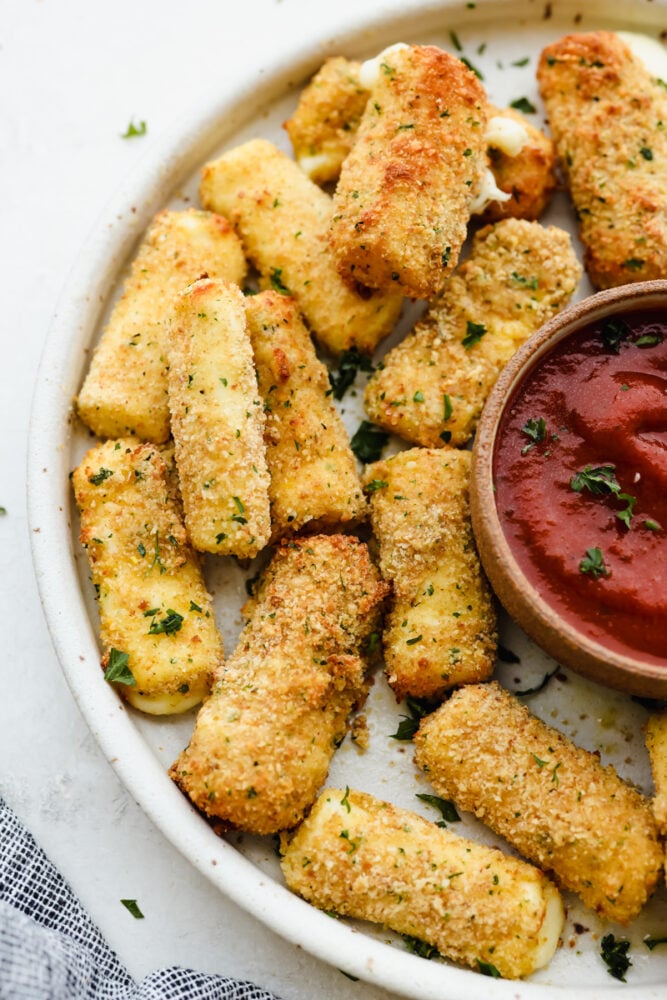 Air fryer mozzarella sticks on a white plate served with marinara sauce.