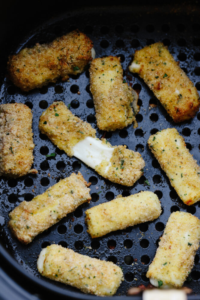 Mozzarella sticks in an air fryer basket.