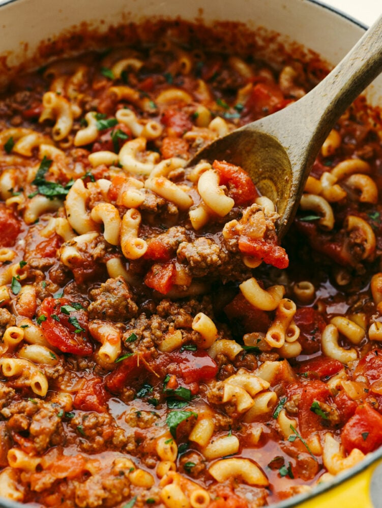 A pot with American goulash being stirred with a wooden spoon.  