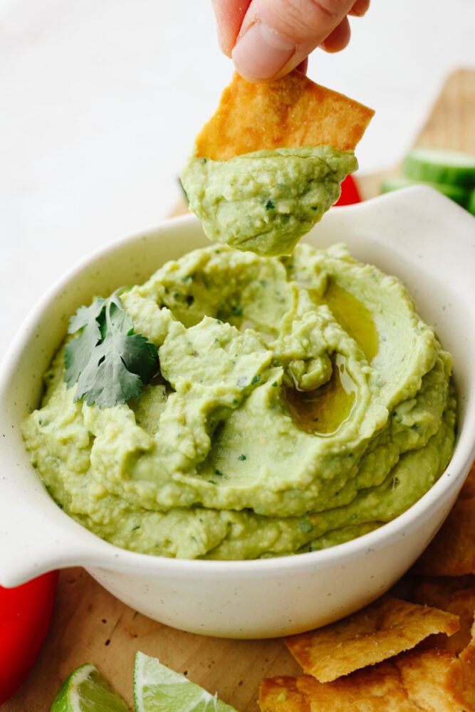 A bowl of avocado hummus being dipped with a pita chip. 