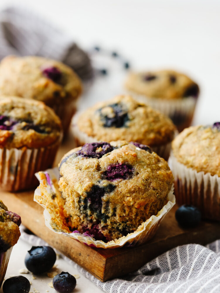 Blueberry muffins on a cutting board, one partially unwrapped.