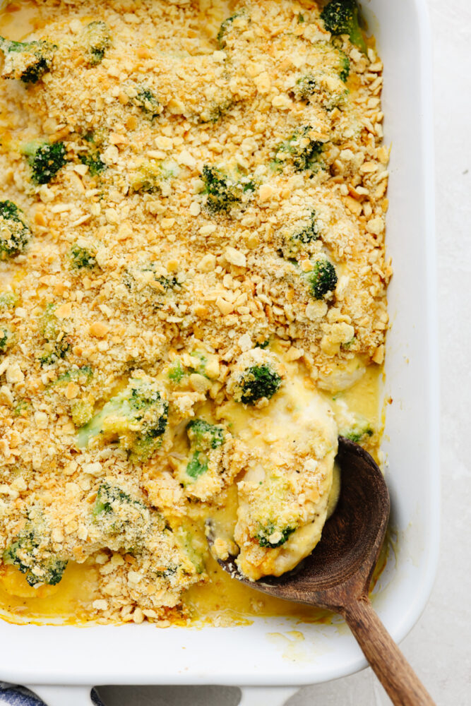 A casserole dish with a wooden spoon serving some broccoli cheddar chicken. 