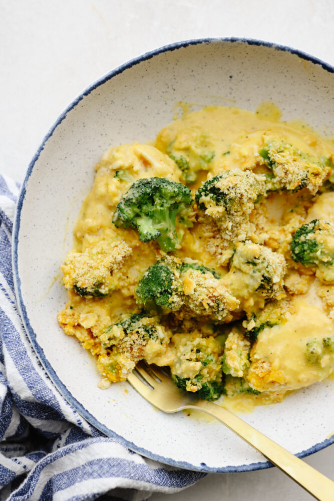 Broccoli cheddar chicken cut up on a plate with a gold fork.