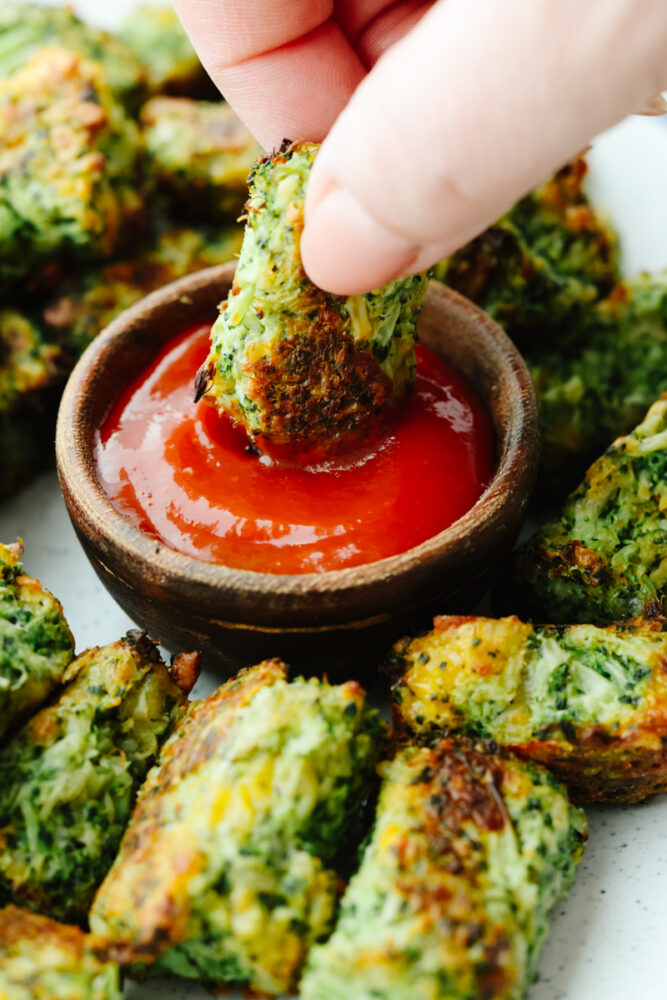 A broccoli tot being dipped into ketchup. 