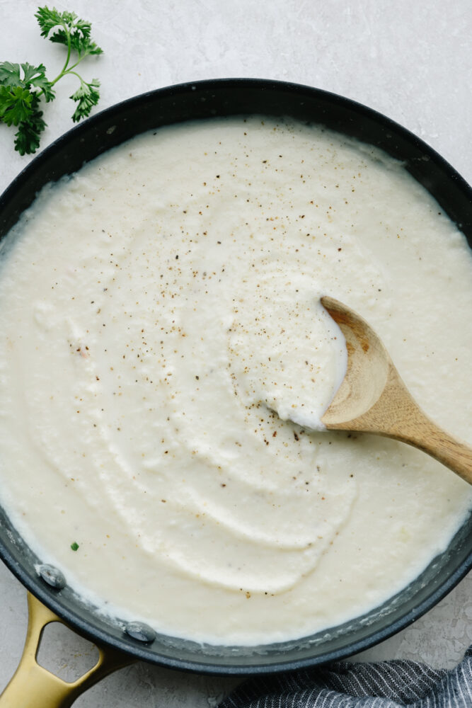 Cauliflower alfredo sauce in a saucepan with a wooden spoon. 