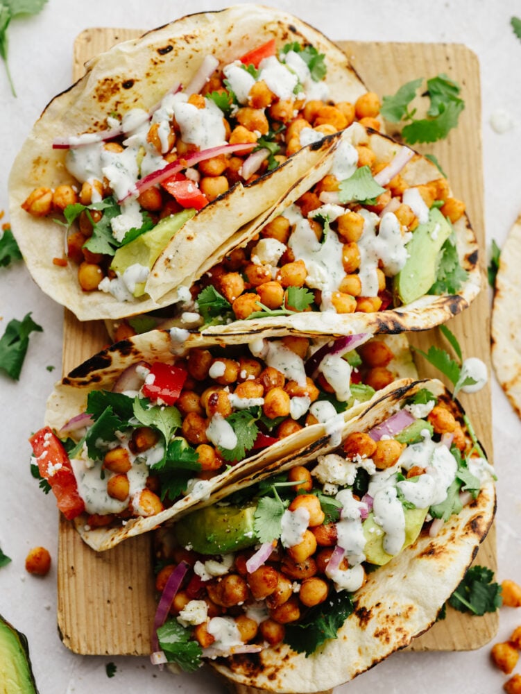 Closeup of 4 chickpea tacos laid out on a wooden board.