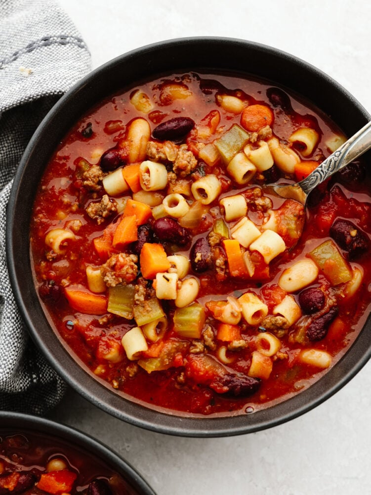 A bowl of pasta e fagioli with a silver spoon. 