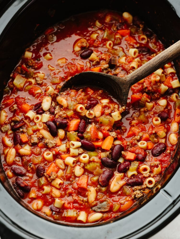 A crockpot of pasta e fagioli with a wooden spoon. 