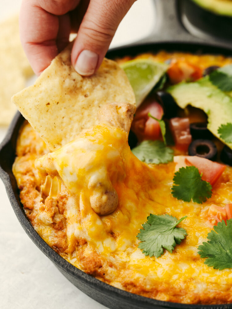 A tortilla chip being dipped into Texas trash dip. 