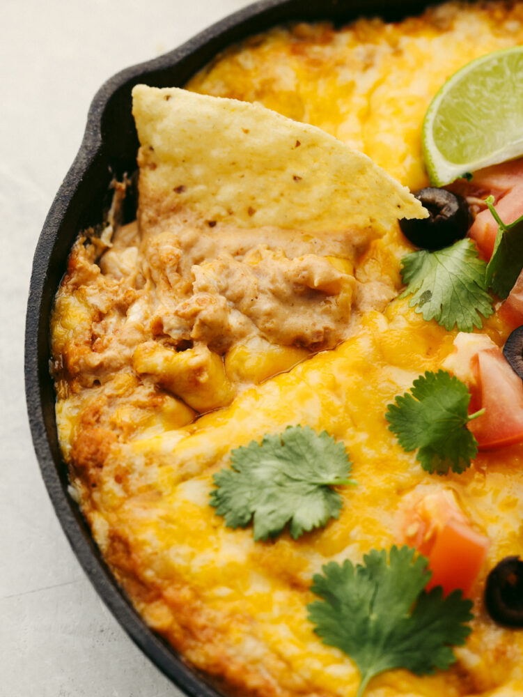 A close up shot of a tortilla chip in a pan of hot bean dip. 