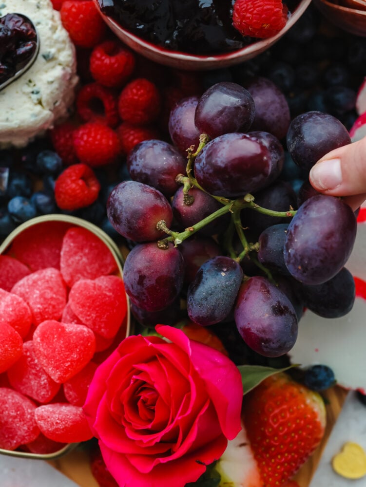 A close up of a hand picking some grapes off of the board. 