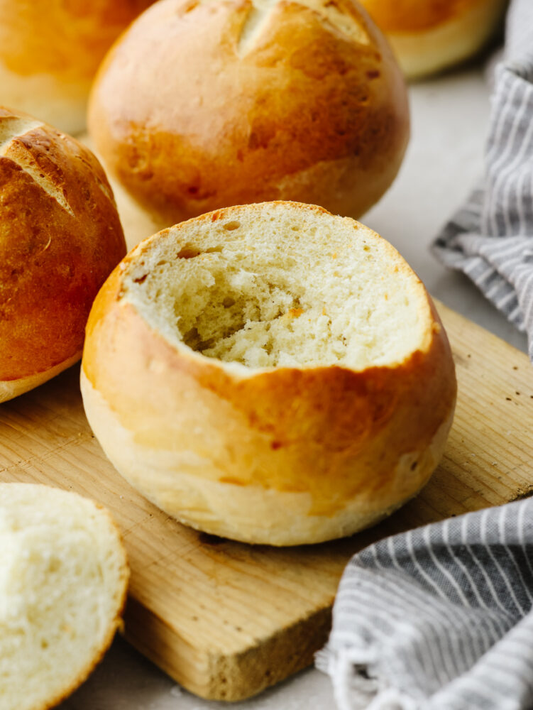 A bread bowl on a wooden cutting board with the top cut out of it, ready for soup! 