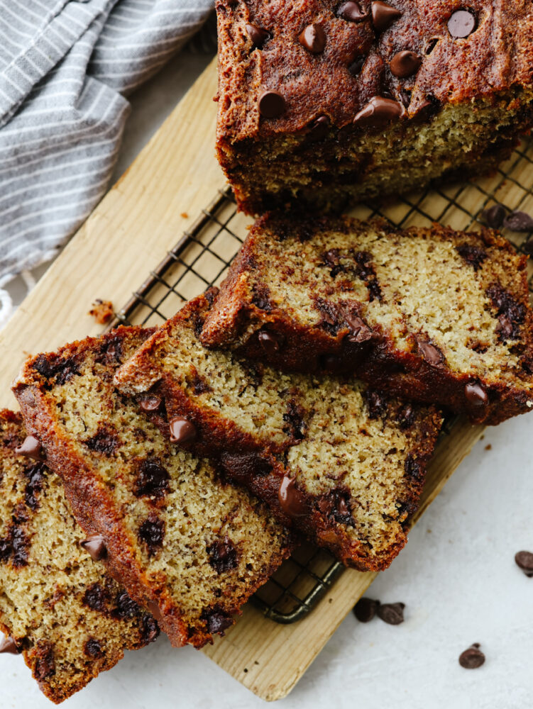 The top view of a loaf of banana bread with a few slices cut on a cooling rack. 