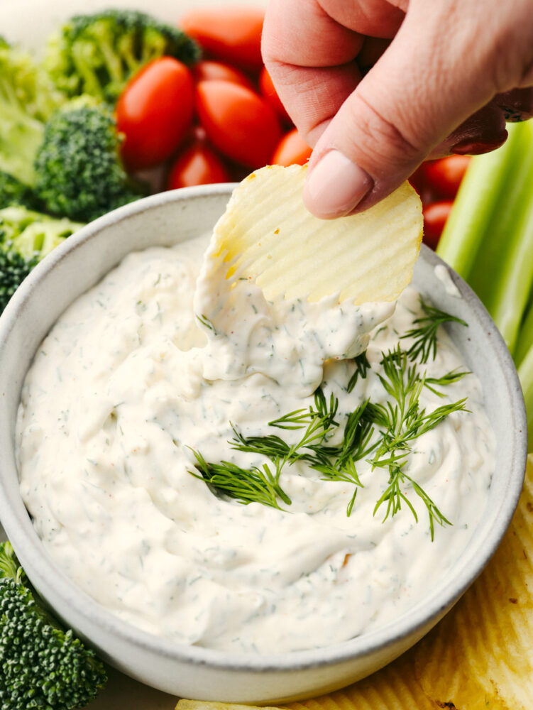 A potato chip being dipped into dill dip. 