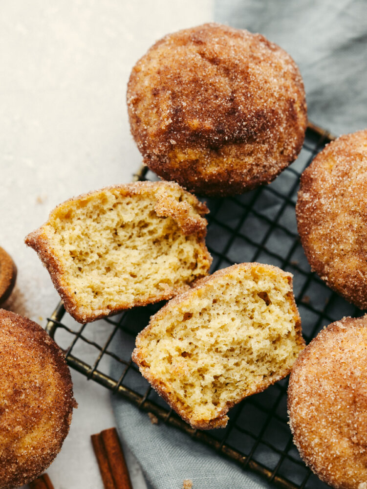 Donut muffins on a cooling rack with one broken in half so that you can see the inside. 