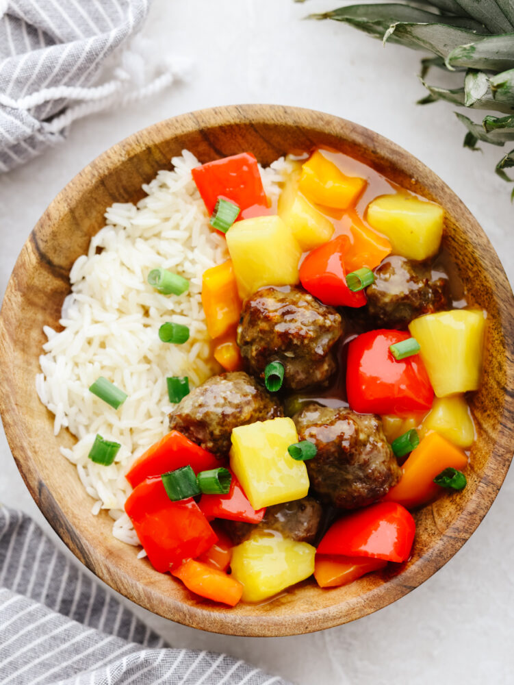 A wooden bowl filled with rice, veggies and meatballs. All garnished with green onions. 