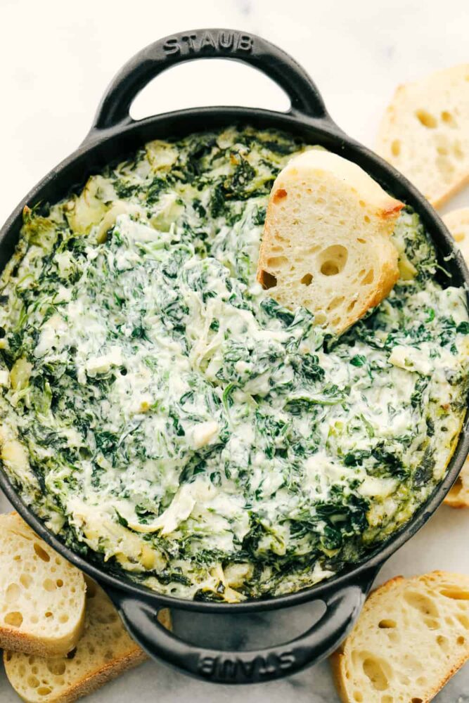 A top view of spinach artichoke dip with a crostini being dipped into it. 