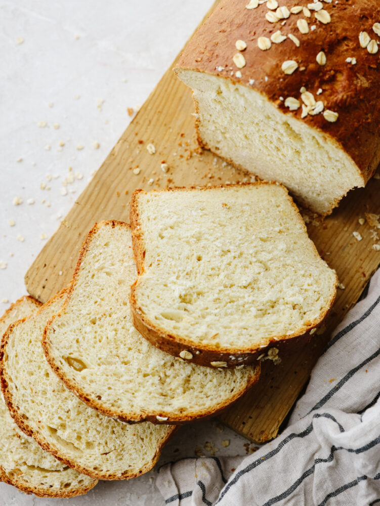 A loaf of oatmeal bread with a few slices on a wooden cutting board. 