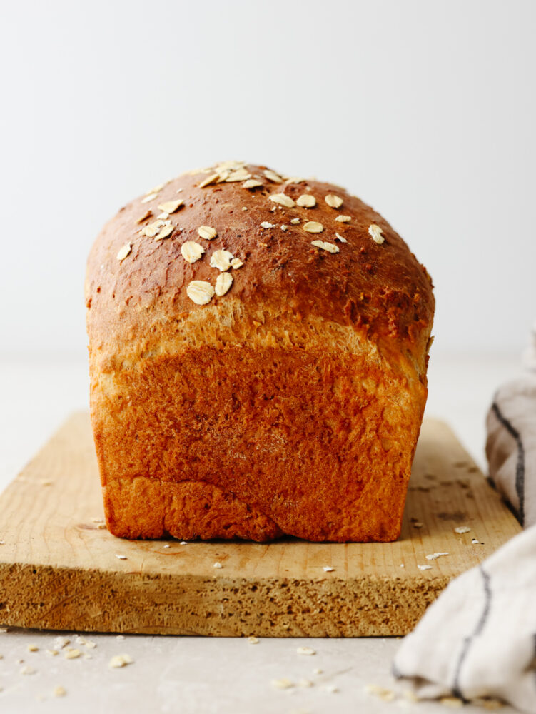 The side view of a loaf of bread on a wooden cutting board. 