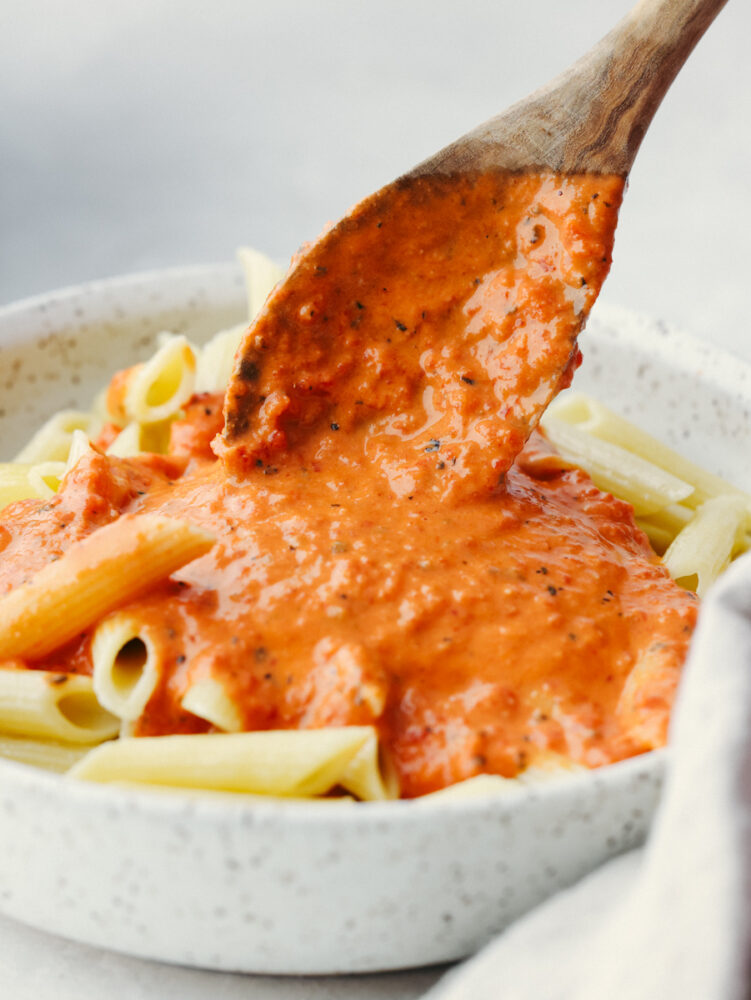 Pouring sauce over penne pasta with a wooden spoon.