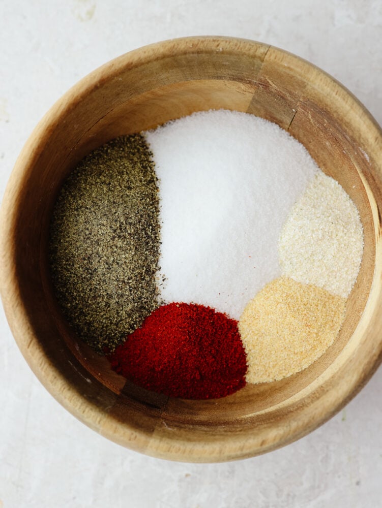 A wooden bowl filled with spices and seasonings, ready to be mixed together. 