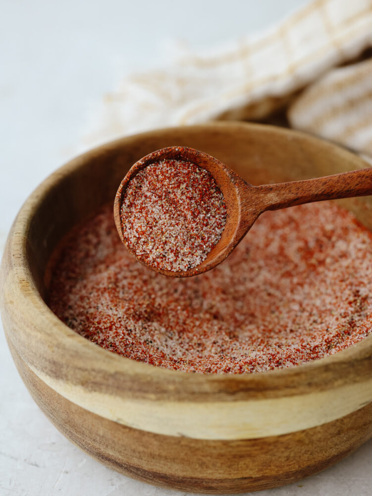 A wooden bowl filled with mixed seasoning salt and being scooped by a wooden spoon. 