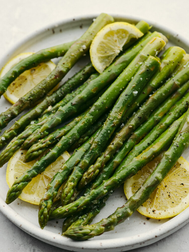 Closeup of steamed asparagus, garnished with salt, pepper, and lemon.