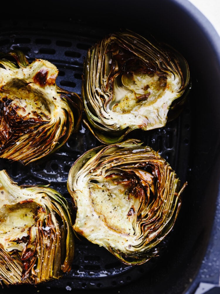 Artichokes cut in half in and air fryer basket. 