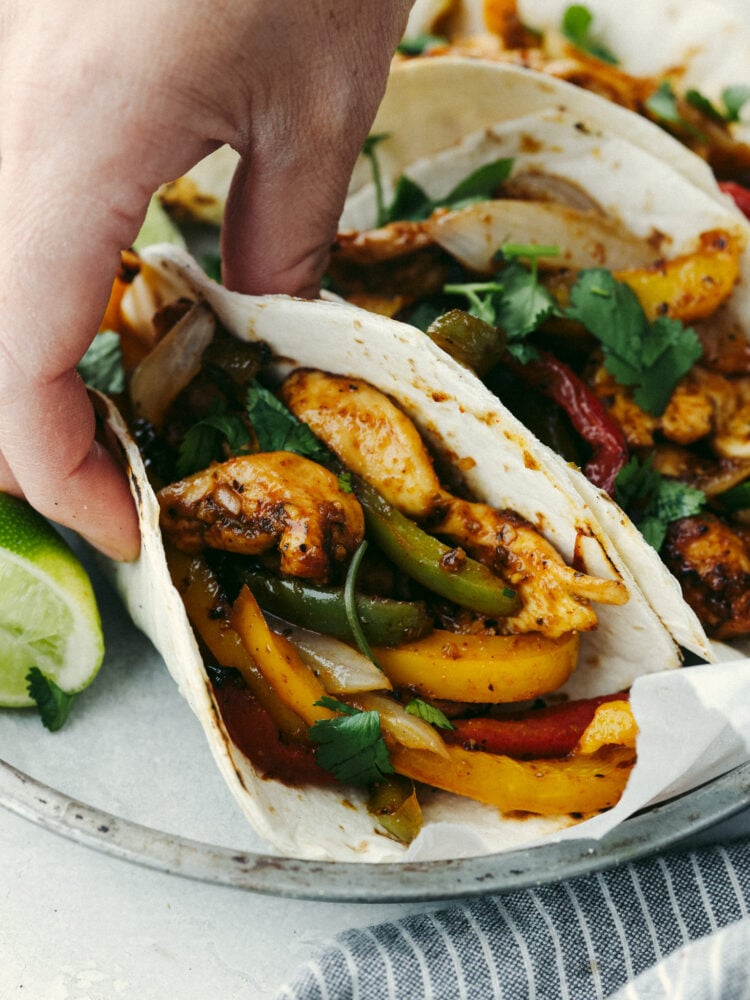 A hand holding and air fryer chicken fajita in an small, flour tortilla. 