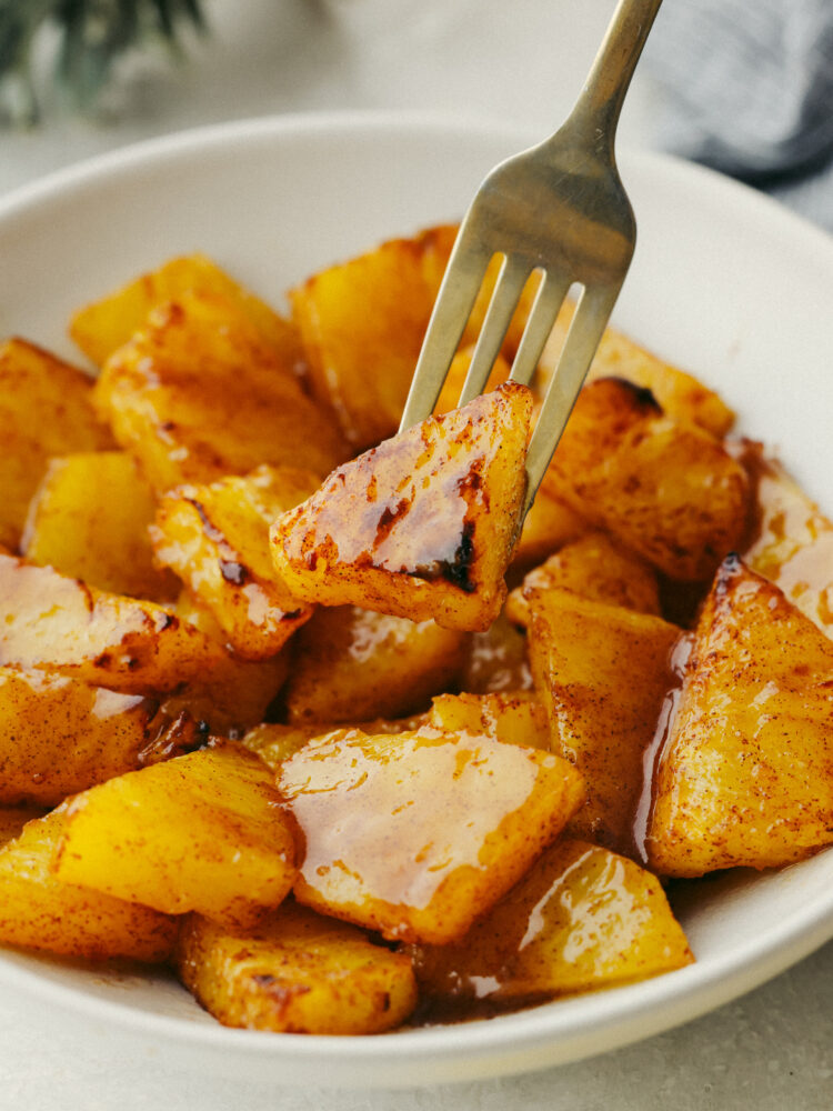 Pineapple with brown sugar glaze in a bowl with a fork biting into a piece. 