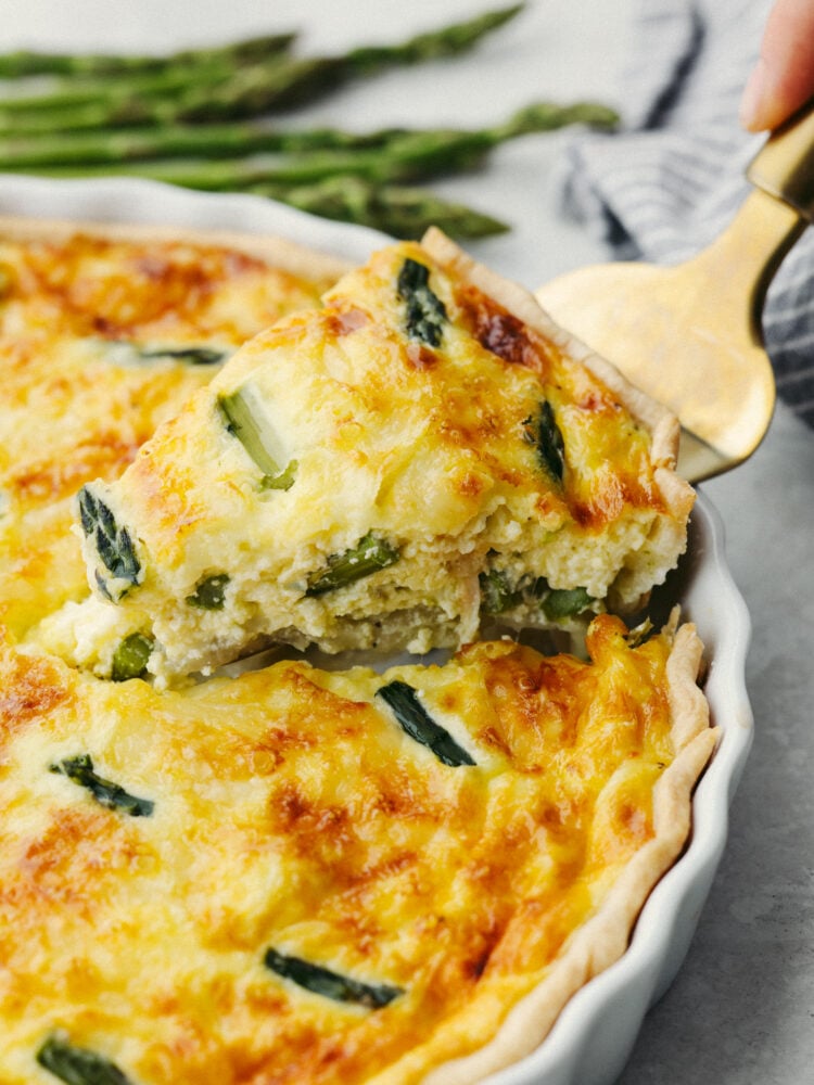 A slice of asparagus quiche being dished out with a gold pie server. 