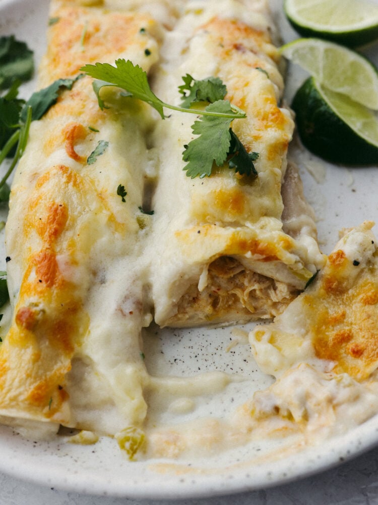 A white chicken enchilada on a plate, half eaten.