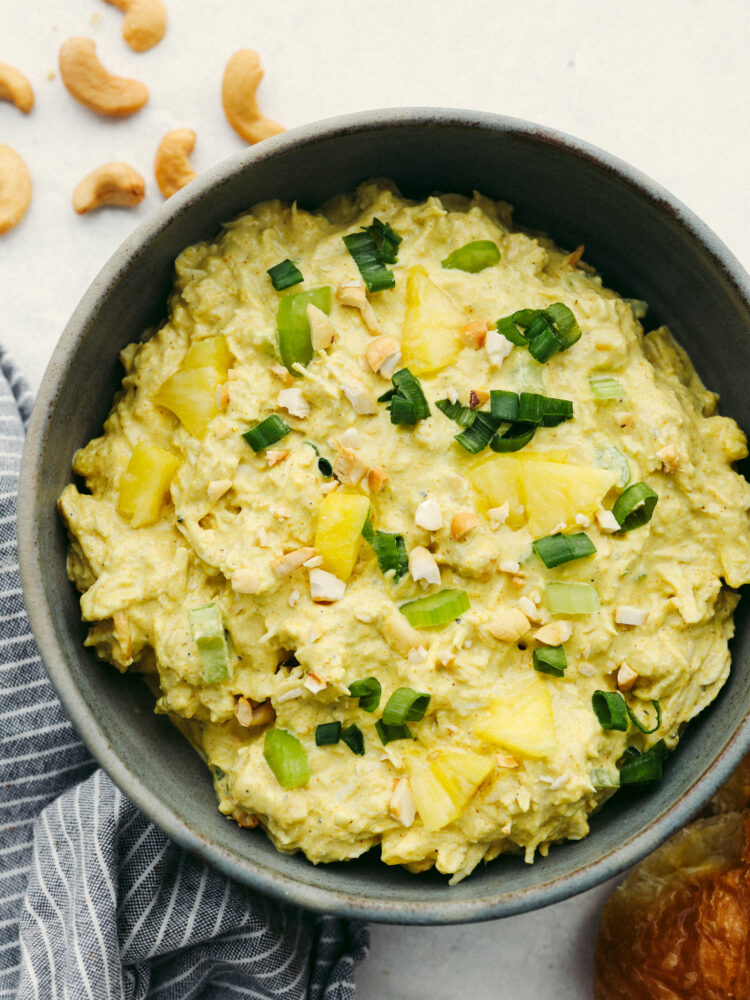 The top view of curry chicken salad in a gray bowl, garnished with cashews and green onions. 