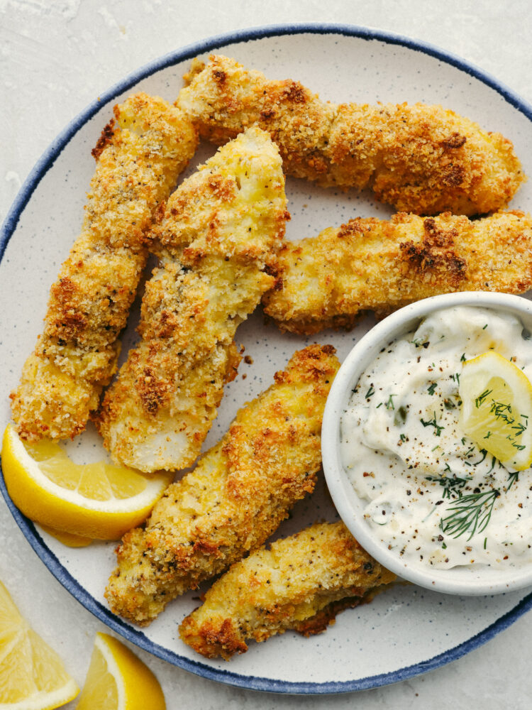 A plate of baked fish sticks and tartar saice. 