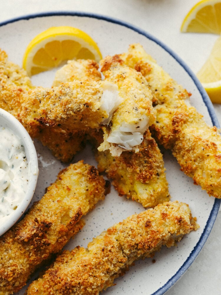 A plate of fish sticks with one broken open so that you can see the flaky fish inside. 