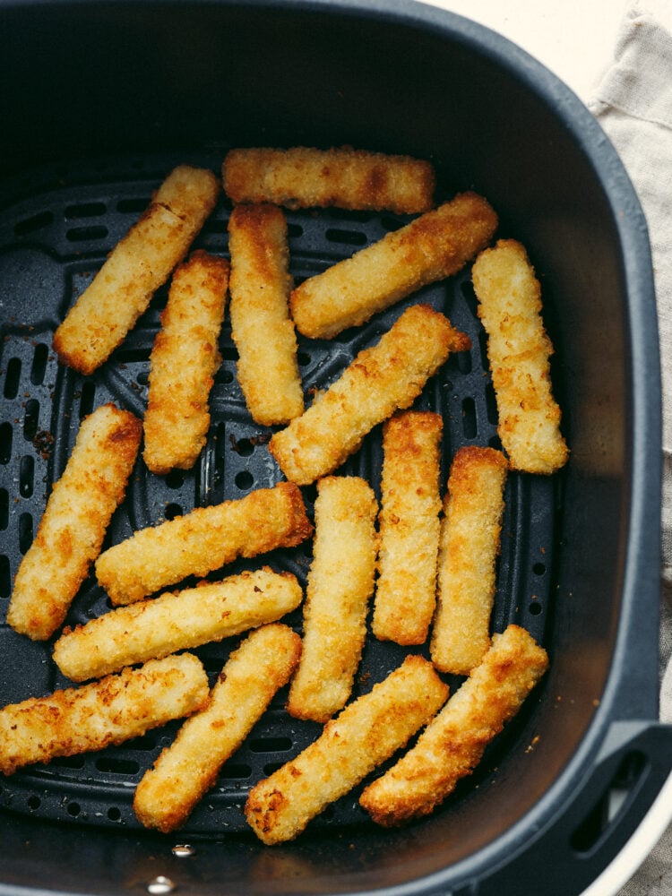 Frozen fish sticks in the basket of an air fryer.