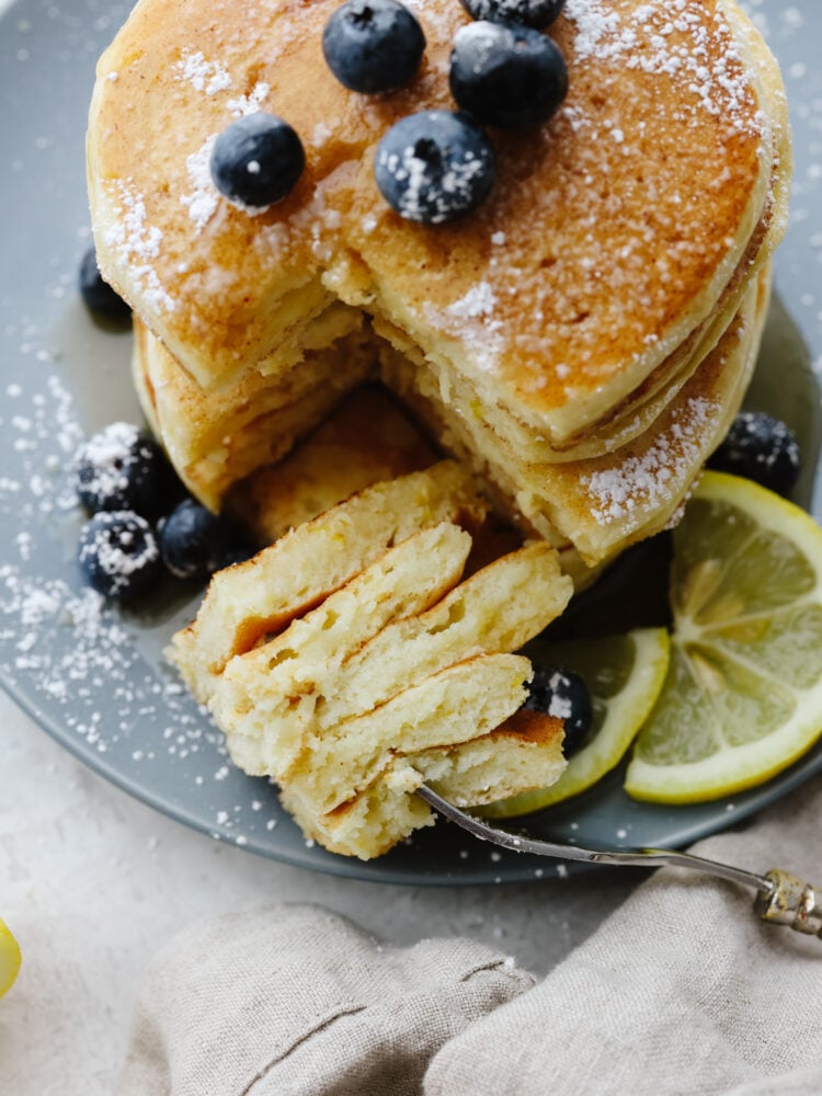 A stack of pancakes on a plate with a triangle cut out with a fork. 