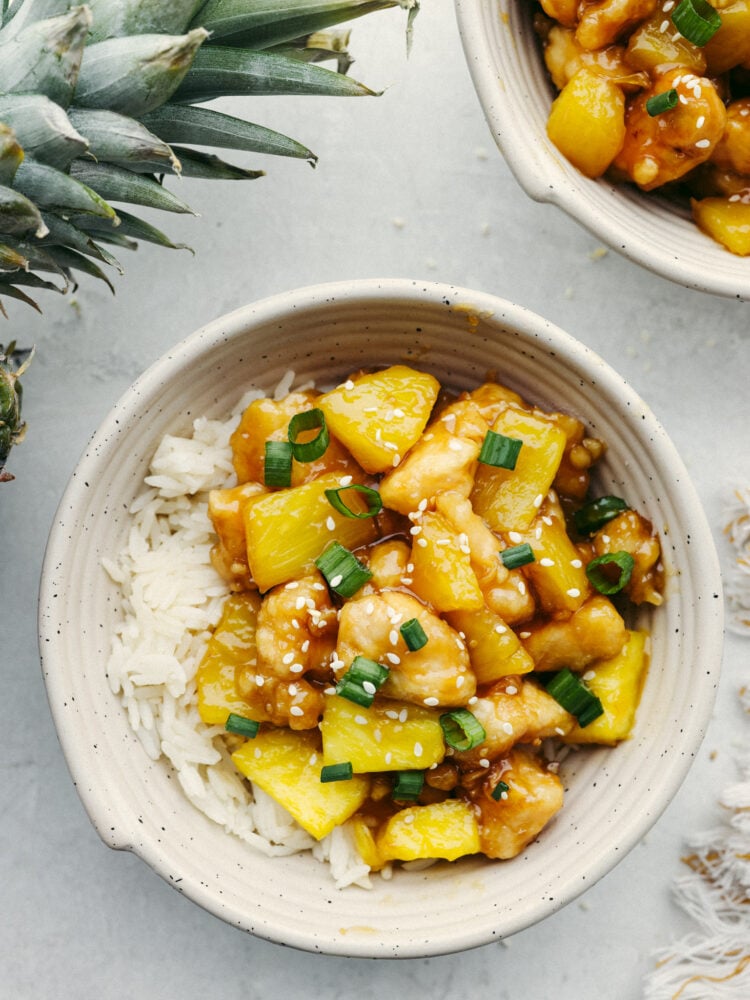 Pineapple chicken served over rice in a white bowl.