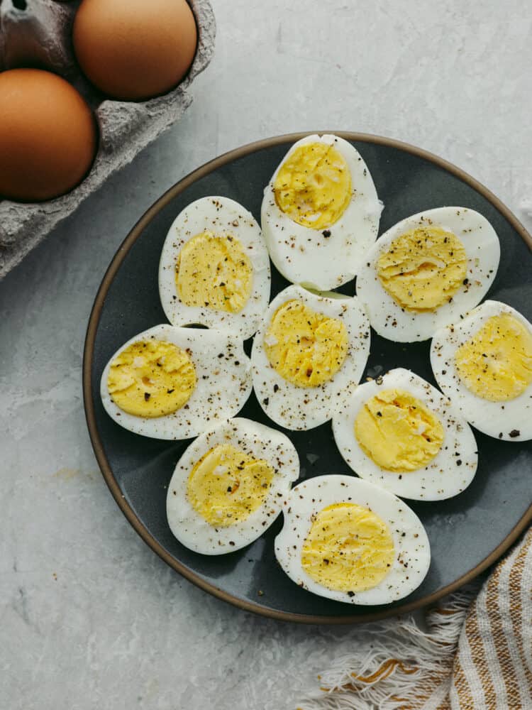 A plate of sliced, hard boiled eggs sprinkled with salt and pepper. 