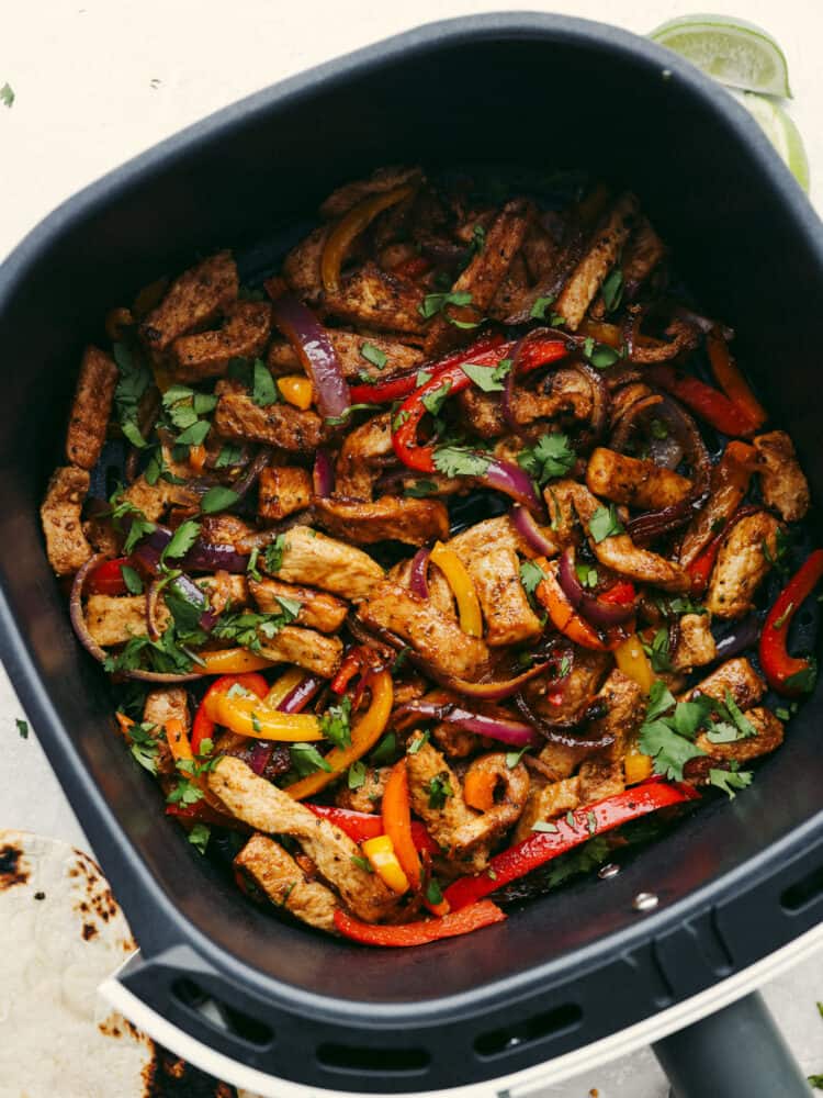 Cooked pork, pepper and onions seasoned in fajita seasoning and in an air fryer basket. 